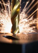 Close-up of a drill cutting into metal with sparks during a high-precision machining process.
